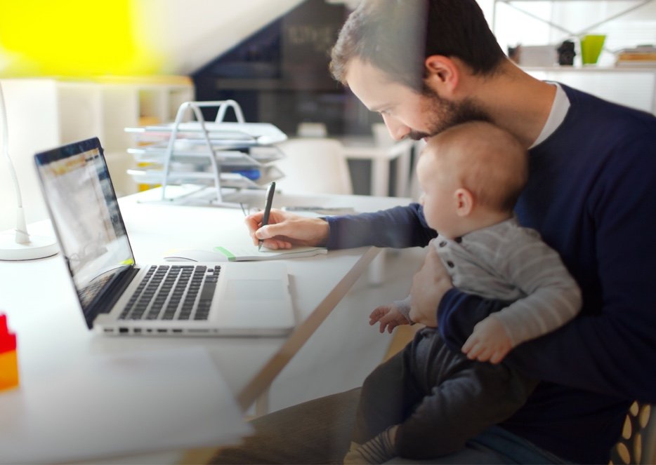 Father completing his online coursework while holding his baby.