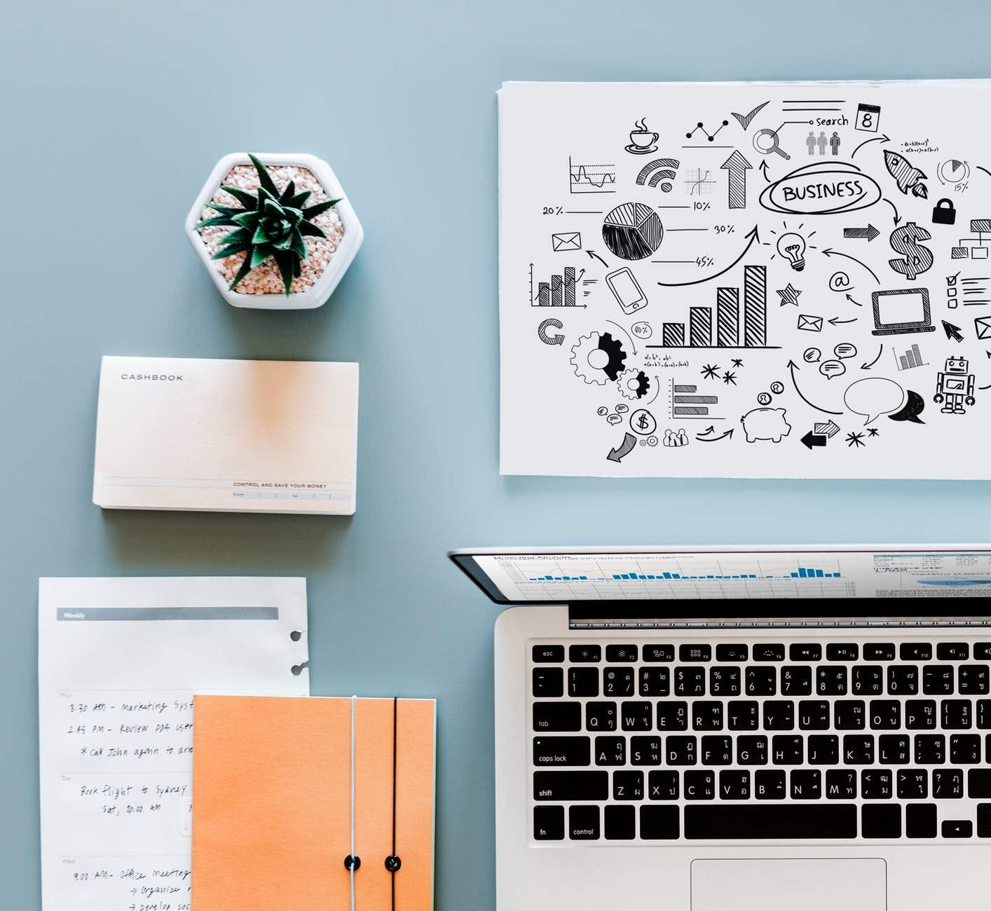 A laptop, notepads, memo pad and cactus on a blue desk
