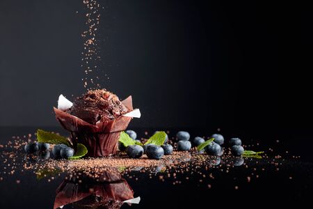 Chocolate muffin sprinkled with chocolate crumbs on a black reflective background. muffin with berries and mint. copy space.