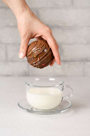 Woman's hand holding tasty cocoa bomb with marshmallows and chocolate that melts when hot milk is added for creating a trendy tasty drink.