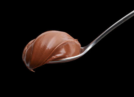 Spoon of melted chocolate hazelnut cream on black background