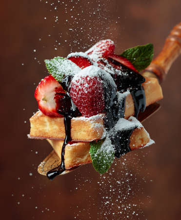 Belgian waffles with strawberries, mint and chocolate sauce, sprinkled with powdered sugar.