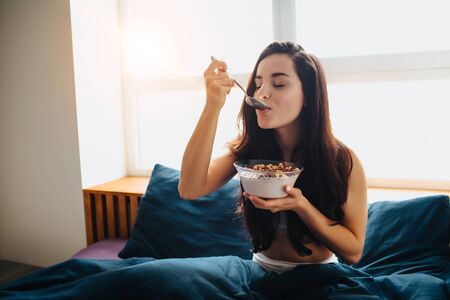 Young beautiful woman in morning bed at home. eating breakfast chocolate cereal bowl with milk. enjoying eating tasty yummy food for morning breakfast.