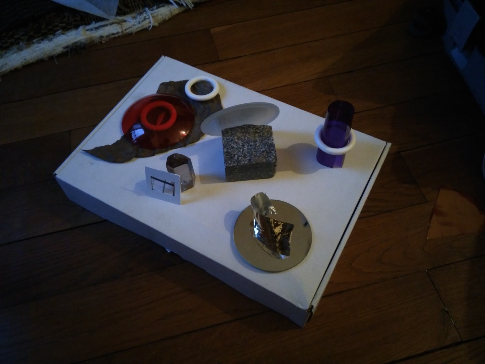monstera - a slide, a leaf, a gold paper, a red transparent thingy, a rock and other objects were left on a white box by Celia Gondol and I - slide, leaf, gold, red plexiglass, rock, white box - paul lahana