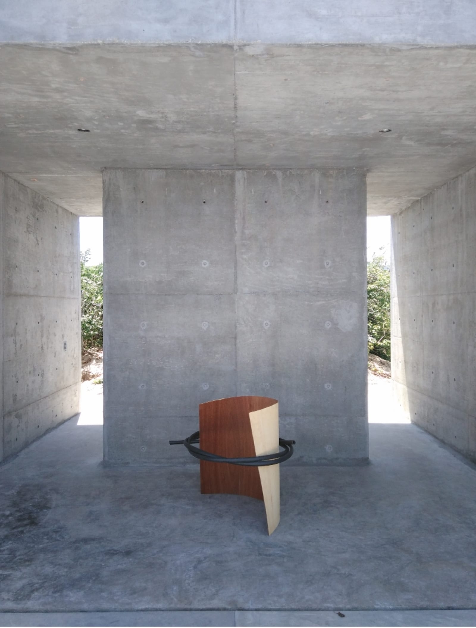 full circle - a thick black plastic tube is holding/embracing a thin wood board in casa wabi - wood, plastic tube - paul lahana
