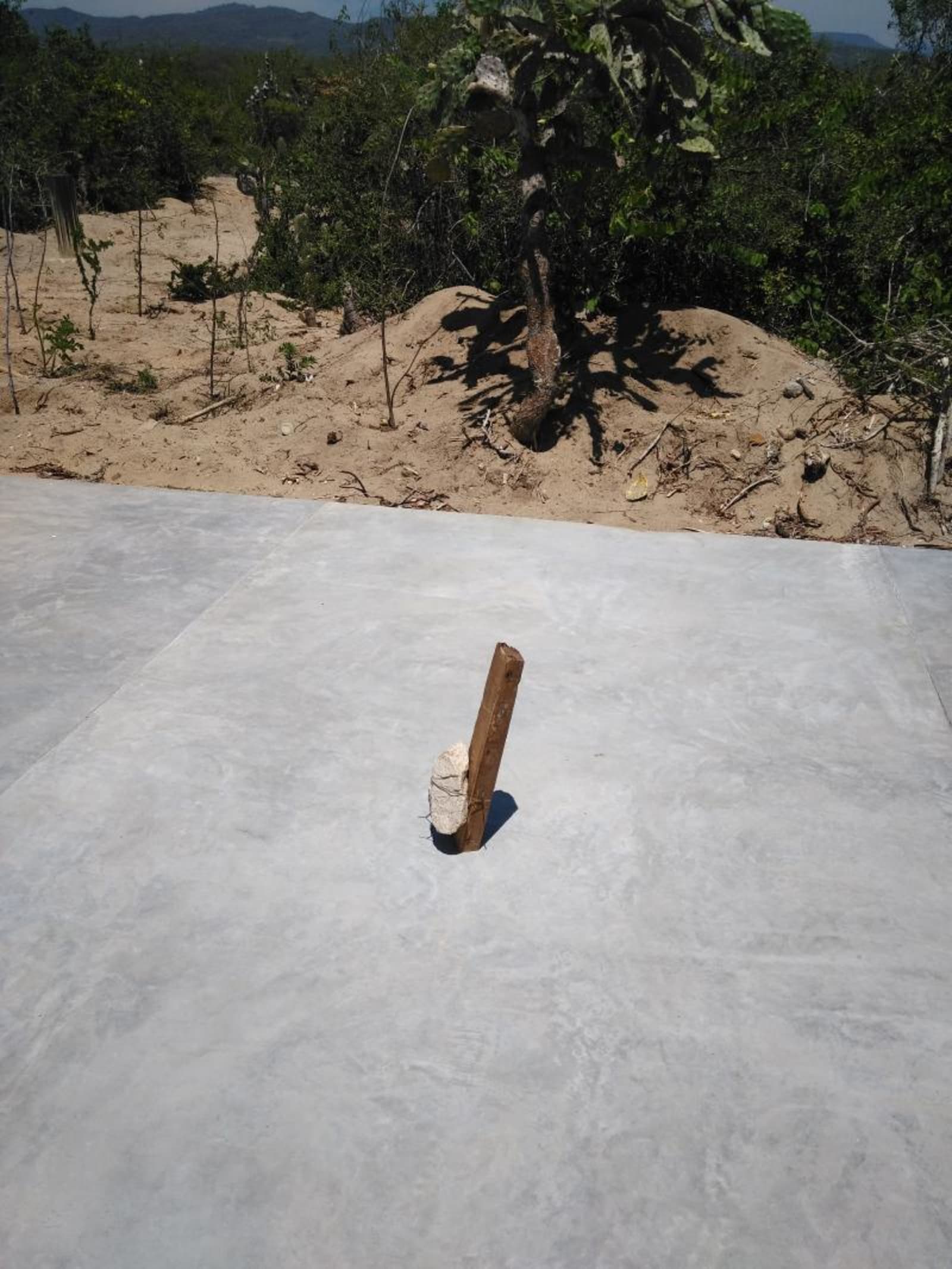 Rockwood - wood piece is holding rock piece on cement floor in casa wabi - rock, wood, cement, iron - paul lahana