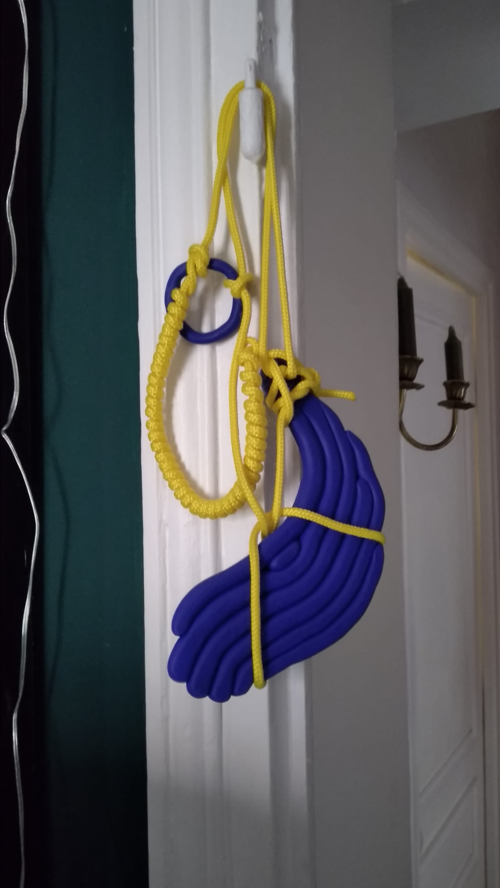 Longue Vue - A blue hand-shapped object is attached with a yellow wire to a white wall - Fimo paste, polyester wire - paul lahana
