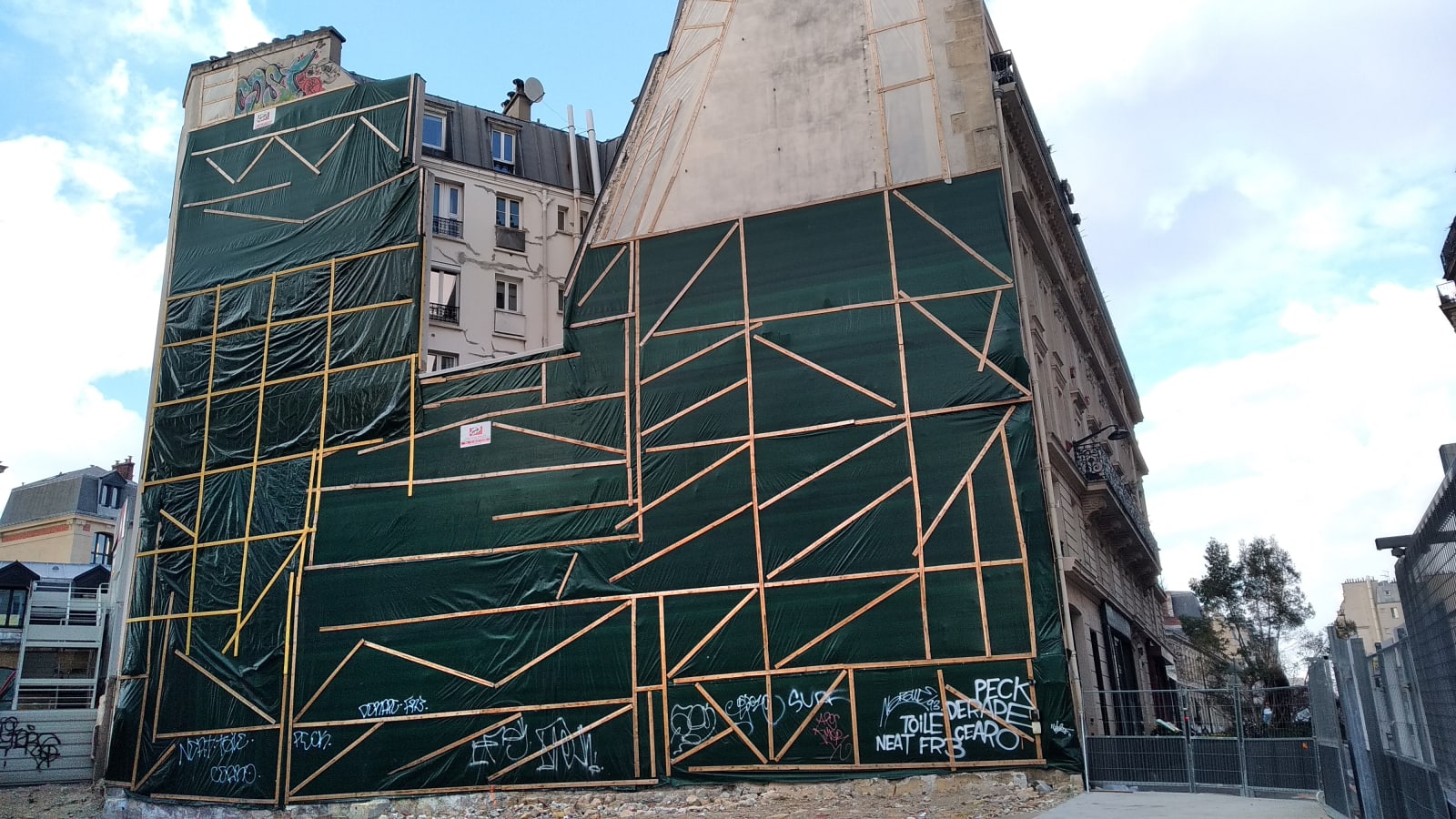 there I fixed it - A building wall is covered with a green plastic layer and is holding thanks to many wood boards - wood, plastic - paul lahana