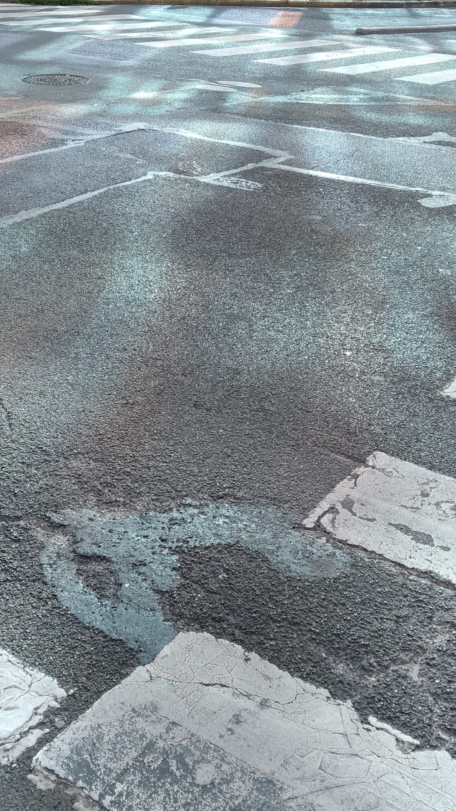 shine bright - A big glass building is reflecting different colors on a tarred road - tar, glass, light - paul lahana