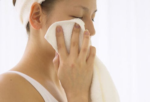 A woman washes around her eye with a washcloth.