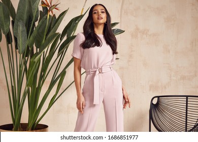 Beautiful sexy brunette woman tanned skin face cosmetic makeup wear pink suit pants for date walk office fashion clothes style collection interior room  sand color safari summer armchair palm boho.