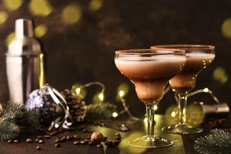 Alexander cocktail in cocktail glass on wooden table with shaker, nutmeg and small grater with christmas decor on dark background. beverage photography. festive cocktail drink.