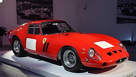 A bright red racing car with blank, square white numbmer patches, on a white showroom platform