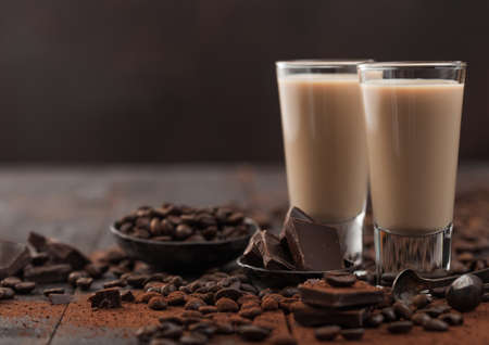 Irish cream baileys liqueur in shot glasses with coffee beans and powder with dark chocolate on dark wood background. space for text