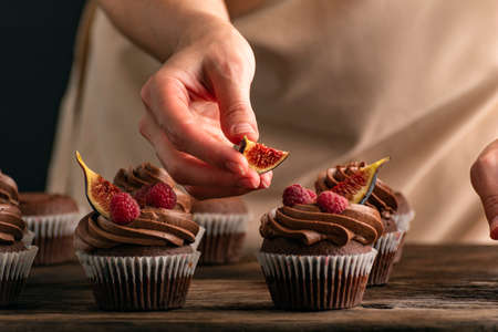 Pastry chef decorates muffins with raspberries and figs. close up of cupcakes preparation Stock Photo