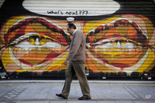 In this photo made on Tuesday, April 29, 2015, a Greek man walks past a graffiti in central Athens. (AP Photo/Petros Giannakouris)