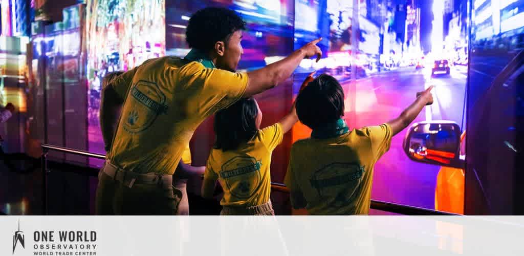Three people in yellow shirts pointing at a vibrant cityscape screen inside an observatory.