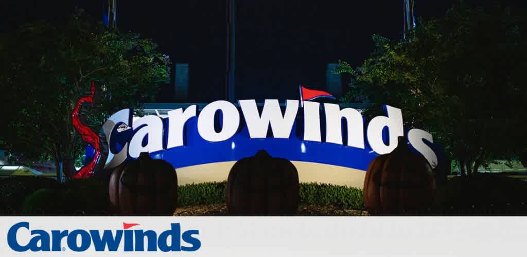 Carowinds entrance sign at night with large white letters and a blue background, featuring a red dragon and pumpkin decorations.