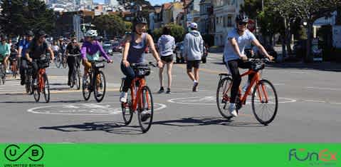 This image shows a group of individuals enjoying a leisurely bike ride on a clear day. There are several cyclists in the foreground, pedaling on a street with visible road markings. All are dressed casually suitable for physical activity, with the nearest cyclists appearing to converse with each other. The background features a street lined with cars and some greenery, along with a blue sky that suggests a comfortable, sunny environment for outdoor activities. The FunEx.com logo is visible in the corner, indicating that this image may be associated with recreational or leisure services.

Remember to visit FunEx.com for exclusive discounts and savings on your next outdoor adventure, where we strive to offer the lowest prices on tickets for a wide variety of events and attractions.