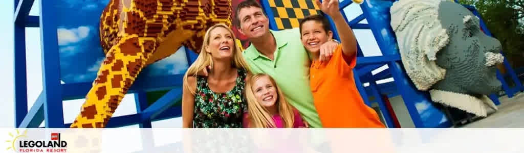 Image showing a joyful family of four with a Lego-themed giraffe sculpture. They are smiling and seem to be enjoying a bright day out at LEGOLAND Florida Resort. The background gives a sense of an amusement park setting. There's a prominent LEGO branding at the top left.