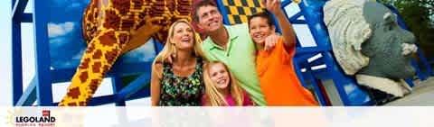 Image displaying a joyful family consisting of two adults and two children with a life-sized giraffe model at LEGOLAND. They are posing together with smiles, and the colorful surroundings suggest a fun and playful atmosphere typical of the theme park.