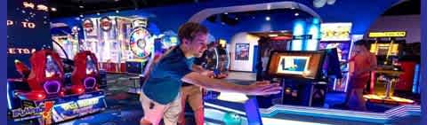 Image Description: This image captures a vibrant indoor arcade setting. The photograph shows individuals engaging in various interactive arcade games. In the foreground, a person with short hair, wearing a dark green polo shirt, is intently playing an air hockey game; they appear to be sliding the puck across a glowing air hockey table. In the midground and background, other colorful arcade games can be seen, featuring bright screens and flashing lights in hues of blue and red. Some individuals appear to be focused on their own games. The venue is well-lit, providing a lively atmosphere for entertainment. 

Remember, by visiting FunEx.com, you can enjoy the thrill of arcade games and more while benefiting from amazing discounts, ensuring you get savings while scouting for the lowest prices on tickets.