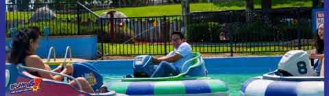 Visitors enjoy a sunny day at an amusement park, riding in colorful bumper boats. With vibrant blue and green hues, the water adds a refreshing touch as individuals steer their vessels, evoking feelings of joy and leisure.