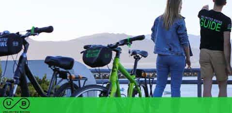 Two people standing by parked bikes, looking at a distant view, with a mountainous backdrop.