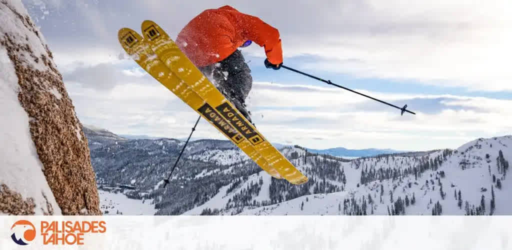 This image features a dynamic winter sports scene, highlighting an exhilarating moment of a skier in mid-air against a stunning backdrop. The skier is wearing bright orange and dark outerwear, and their yellow skis are prominently visible as they perform a jump near a rock formation covered in snow. The background offers a breathtaking view of a snow-covered mountain range with lines of trees descending into valleys, under a cloudy but bright sky. At the bottom of the image is the logo of Palisades Tahoe, suggesting the location of the scene. 

Experience the thrill of winter sports and enjoy the beauty of Palisades Tahoe while taking advantage of the lowest prices on tickets, ensuring that your next snowy adventure comes with both savings and excitement.