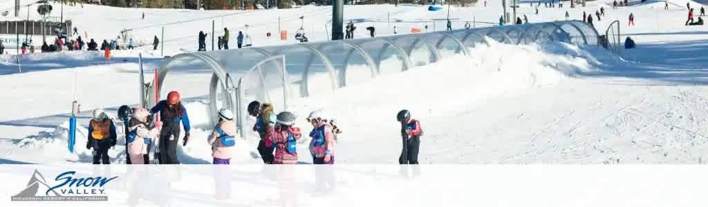 Image Description: This panoramic winter scene showcases the bustling activity at Snow Valley ski resort. A bright, clear sky oversees the sparkling white slopes where an array of skiers and snowboarders dot the landscape. Visitors are gathered at the base of the hill, some preparing to ascend on a covered conveyor belt lift, commonly known as a magic carpet, which is situated on the left side of the image. Individuals of varying ages and ski attire are visible, including children with colorful helmets and adults adjusting their equipment. The Snow Valley logo is prominently featured in the bottom left corner, solidifying the location and the spirit of winter sports prevalent in the scene. 

Remember, when you book with FunEx.com, you're guaranteed to enjoy the excitement of winter sports with the added bonus of incredible savings on tickets. Get ready for an adventure on the slopes at the lowest prices available!