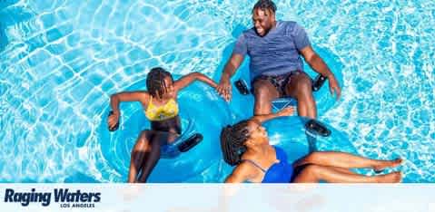 Image features three people enjoying a water park slide, sitting on inner tubes. They are surrounded by vibrant blue water with light patterns reflecting off the surface. The water park is identified as Raging Waters, Los Angeles. The atmosphere is lively and fun.