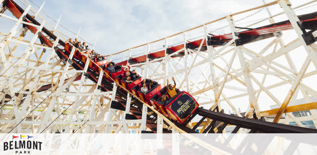 This image displays a scene of vibrant amusement, captured at Belmont Park. A traditional wooden roller coaster, with red tracks and a white support structure, dives steeply downwards, delivering a thrilling experience to the passengers securely seated in the open-top cars. The clear sky suggests it's a bright and cheerful day, perfect for outdoor activities. The roller coaster car nearest to the camera prominently features the text "Belmont Park" in stylized lettering, reinforcing the identity of the amusement park. The excitement and enjoyment of the riders are palpable as they descend the slope, hands raised in exhilaration.

At FunEx.com, we are committed to bringing you the lowest prices on tickets, ensuring that your next adventure is filled with joy and savings.