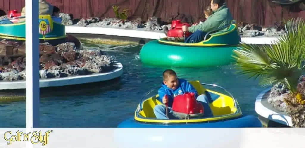 Image Description: The image showcases an outdoor bumper boat attraction at an entertainment venue named 'Golf N' Stuff'. We see individuals seated in colorful, circular bumper boats equipped with water cannons. The boats float in a sizeable pool area surrounded by themed landscaping, such as faux boulders and a palm tree. In the foreground, a joyful child in a blue and yellow boat appears to be steering with enthusiasm, while in the background, another individual in a predominantly green boat proceeds calmly across the water. There's a clear sky suggesting it is a sunny day, ideal for this kind of outdoor activity.

At FunEx.com, we're committed to bringing you unbeatable savings on tickets to your favorite attractions, ensuring you get the lowest prices for endless fun!