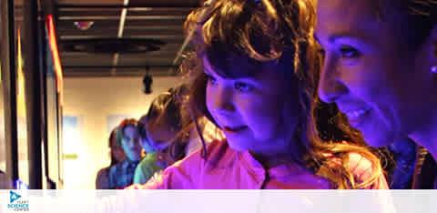 This image depicts a cheerful indoor scene with two individuals prominently featured in the foreground, experiencing a visually engaging exhibit. On the left is a young child with an expression of delight and curiosity, looking down towards a lit display, illuminated by a purple-hued light which highlights the contours of their face. Adjacent to the child, on the right, is an adult with a joyous smile, evidently enjoying the shared moment, as they look towards the child with a sense of wonder and camaraderie. In the background, other attendees are present, subtly blurred, which suggests a busy and interactive environment. The setting appears to be dynamic and family-friendly, designed to capture the imagination of its visitors.

Remember, when planning your next family adventure, visit FunEx.com for exclusive discounts, savings on tickets, and enjoy the lowest prices on a wide array of fun experiences!