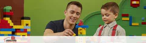 Banner image featuring a smiling adult male and a young boy with toys. They appear to be playing with colorful building blocks on a table. The backdrop includes a wall adorned with block-like designs, indicating a playful, creative setting. The logo for LEGOLAND is visible in the corner, suggesting the theme of the environment.