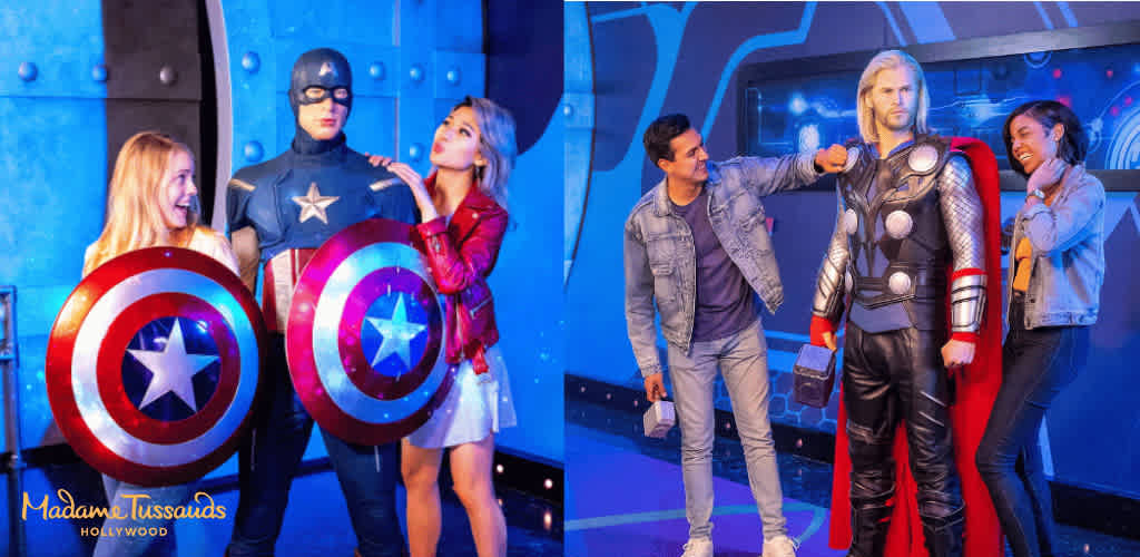 Group of people with costumes and props at a superhero-themed entertainment attraction with Madame Tussauds Hollywood branding visible.