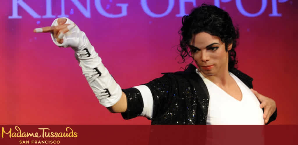 Image description: A life-like wax figure representing an iconic pop star poses against a vibrant pink background with the text "KING OF POP" prominently displayed. The figure is outfitted in a classic black jacket sprinkled with shimmering sparkles over a plain white V-neck shirt. A signature white glove adorned with black accents and embellishments covers the figure's right hand, which is extended towards the viewer in a dynamic, pointing gesture. Natural-looking black curly hair frames the figure's face, enhancing the faithful recreation of the star's well-known looks and on-stage charisma. The figure appears at Madame Tussauds in San Francisco, as indicated by the logo in the lower left corner of the image.

Explore the wonders of Madame Tussauds on FunEx.com and enjoy the amazing savings we offer with our exclusive discounts, ensuring you get the lowest prices on tickets to meet the stars.