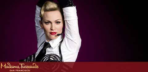 This image features a promotional banner from Madame Tussauds in San Francisco. It showcases a life-like wax figure of a woman styled as a classic pop star, posing with her hands holding the top of her head and elbows angled outward. The figure is dressed in a white blouse with a black vest and features stylized makeup, including red lipstick. The background of the photo is a striking purple which gradients to a deeper shade towards the edges, putting an emphasis on the figure at the center. The Madame Tussauds logo is prominently displayed at the bottom left of the image.

For those planning a visit to Madame Tussauds in San Francisco, make sure to check FunEx.com first for exclusive discounts and the lowest prices on tickets.