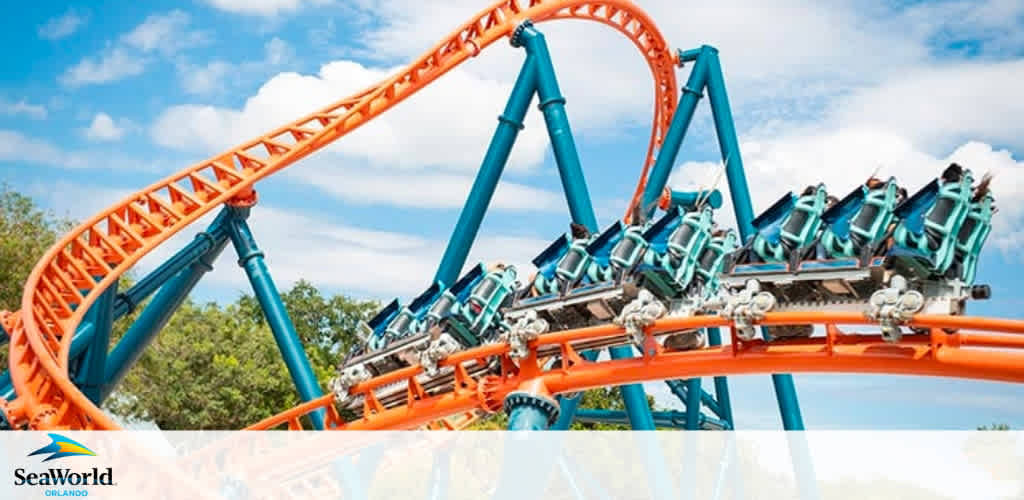 Image shows an orange roller coaster with blue supports, climbing an incline under a clear sky. Below the coaster, a logo for SeaWorld Orlando is visible, suggesting the location. Riders appear secured in their seats, enjoying the ascent.