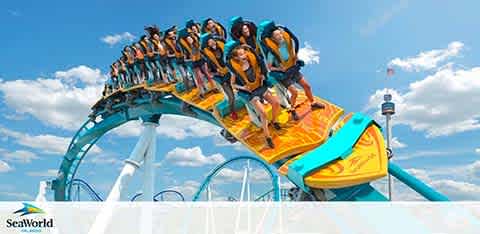 Image displays a bright blue roller coaster with an orange track at SeaWorld. A group of excited riders, securely harnessed, crest the top of a loop with arms raised. White clouds scatter across a vibrant blue sky, suggesting a perfect day for thrill-seekers at the amusement park. SeaWorld's logo is visible in the corner.