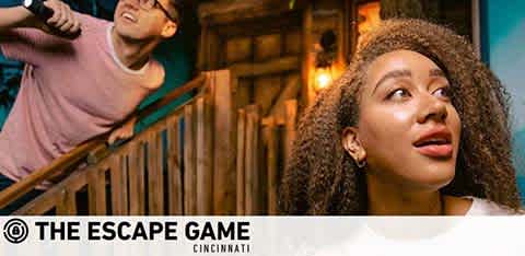 Image of two excited individuals at The Escape Game Cincinnati. A man in the background is reaching upward with glee, and a woman in the foreground looks away thoughtfully. Both appear engaged and entertained. The logo of The Escape Game is prominent at the bottom.