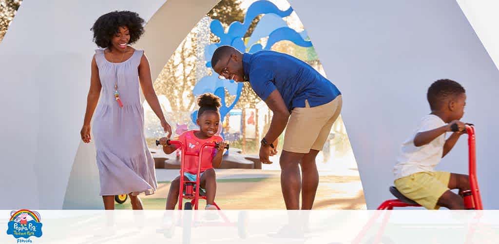 Family enjoys a sunny day at a playground with kids on toy bikes.