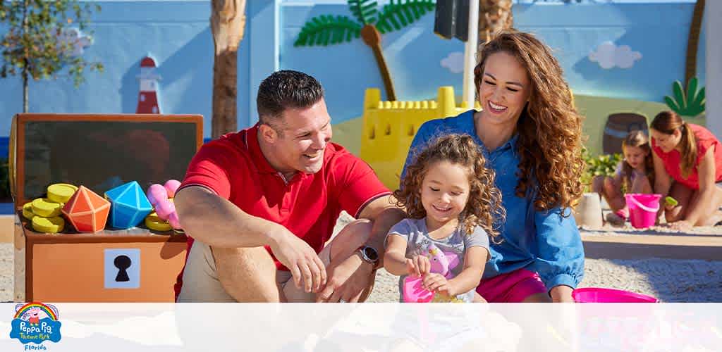 Family enjoys playtime at a sandpit with toys, sunny backdrop, promoting Peppa Pig theme.