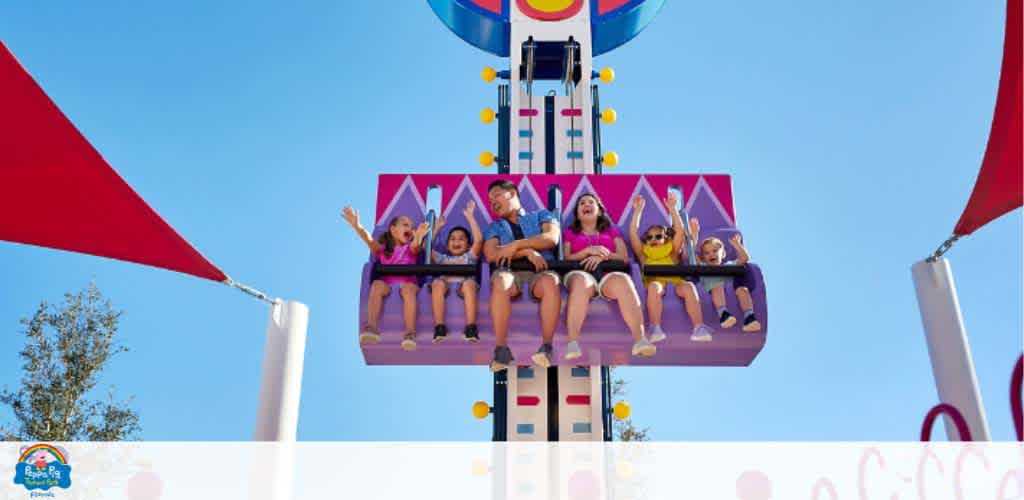 People on a drop tower ride at an amusement park, excited and raising their hands.