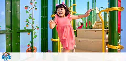 Young girl in pink dress happily playing on colorful playground.