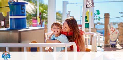 Woman and child smiling on a sunny amusement park ride.