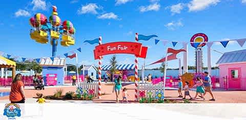 A colorful fun fair entrance with people, balloon ride, and blue sky.