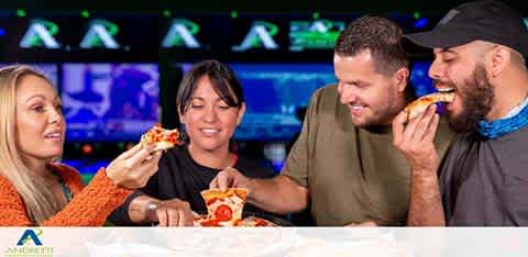 Four friends enjoy pizza together in a lively arcade setting.