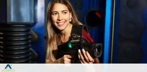 Woman smiling, holding a laser tag gun, ready to play in an arena.