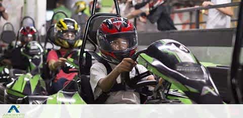 People in helmets driving go-karts indoors, focused and ready to race.